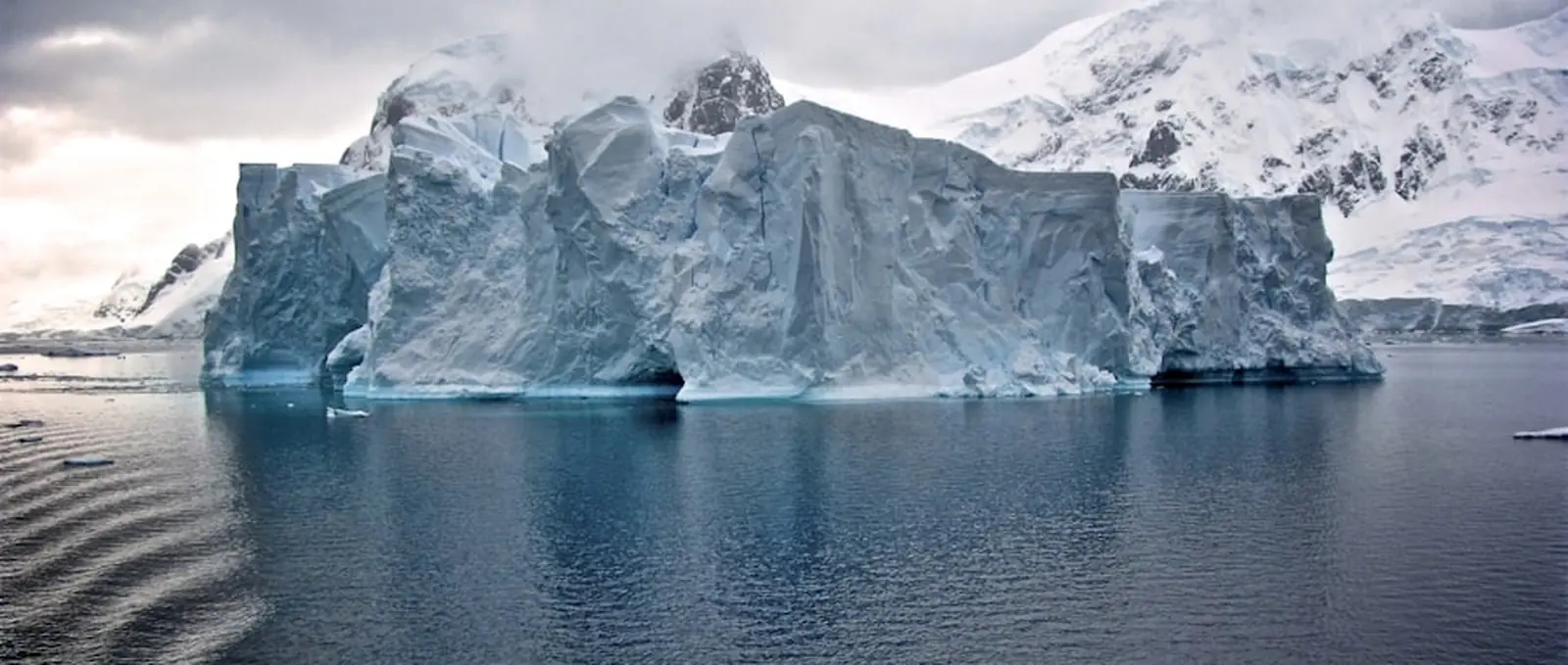 An iceberg in dark water under a heavy sky.