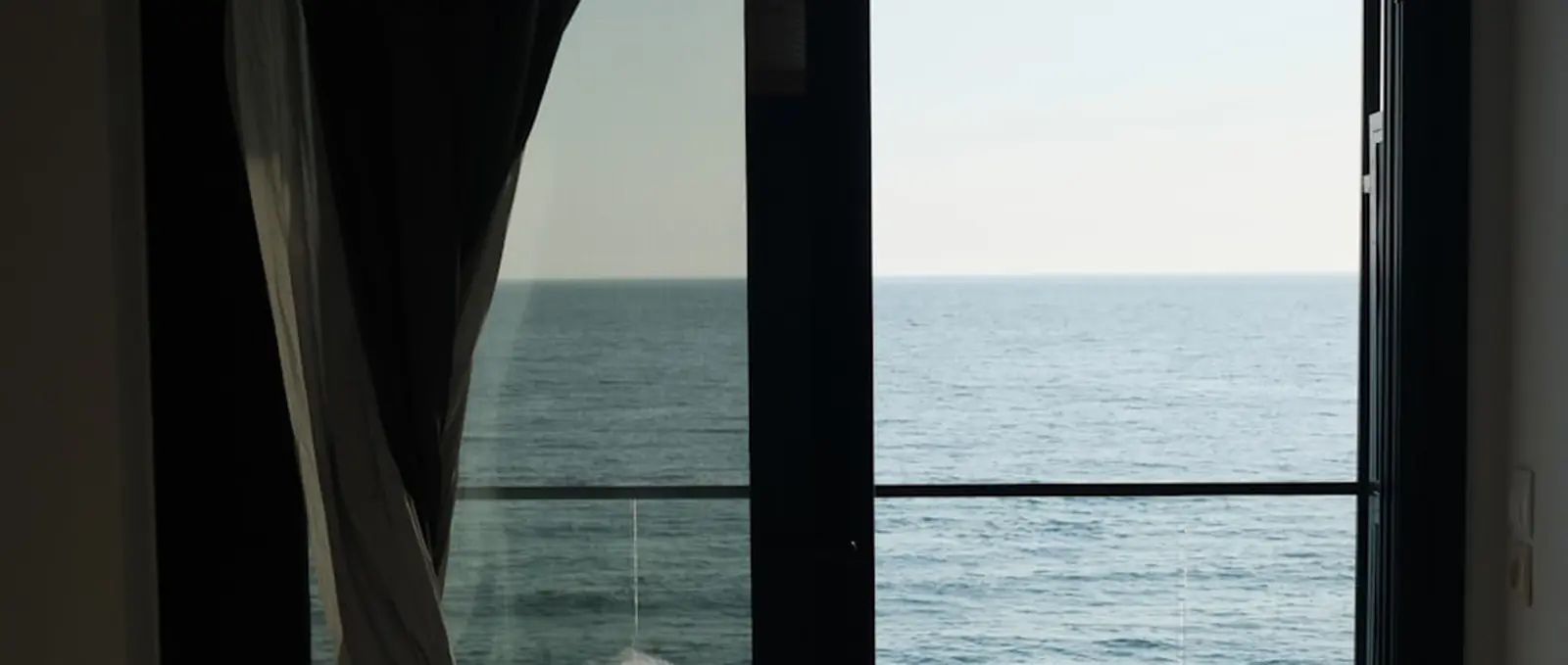 A room opening onto the sea, curtain drawn back.
